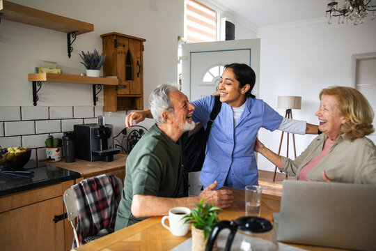 Caregiver greeting senior couple in home kitchen