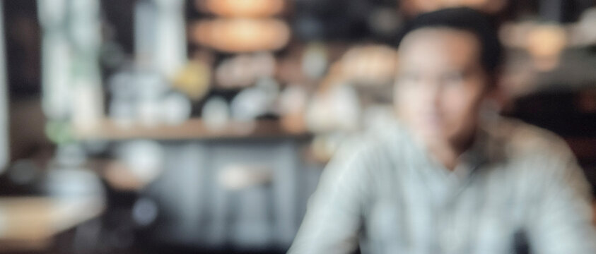 A blurred image of a person sitting in a caf&eacute;, with an indistinct background featuring warm lighting and a lively atmosphere.