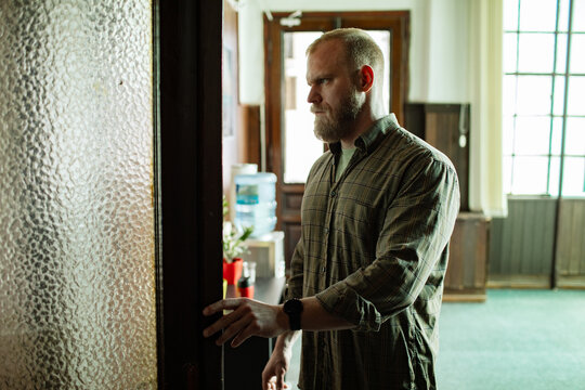 Bearded man opening frosted glass door in office