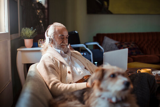 Senior man with headphones using laptop at home