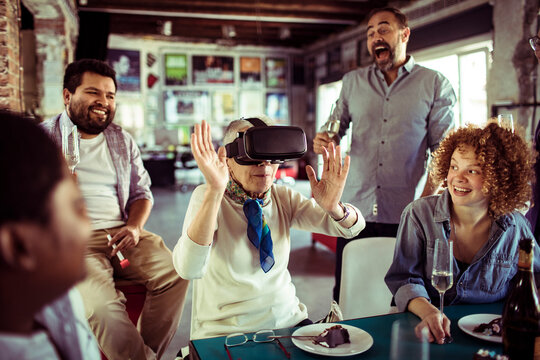 Senior woman exploring virtual reality with friends at casual party