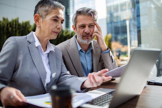 Senior business colleagues reviewing data on laptop outdoors