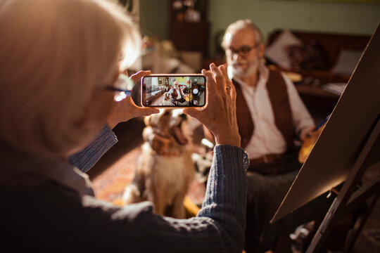 Senior woman photographing man painting with dog at home studio