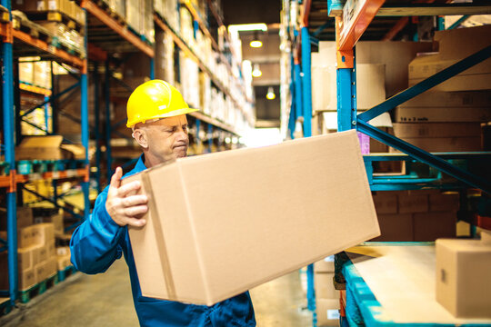 Warehouse worker lifting heavy box in storage aisle