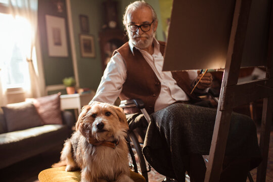 Senior man in wheelchair painting at home with dog
