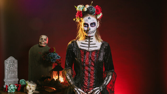 Spooky goddess of death with skull make up and horror costume to celebrate dios de los muertos on mexican halloween. Creepy woman dressed as santa muerte on day of the dead holiday.