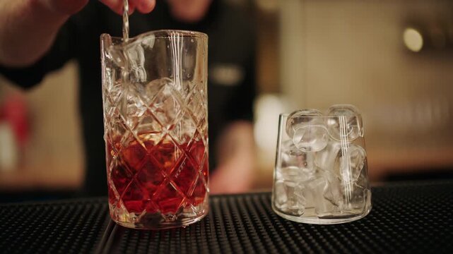 Close up of a bartender stirring a cocktail with ice in a crystal mixing glass