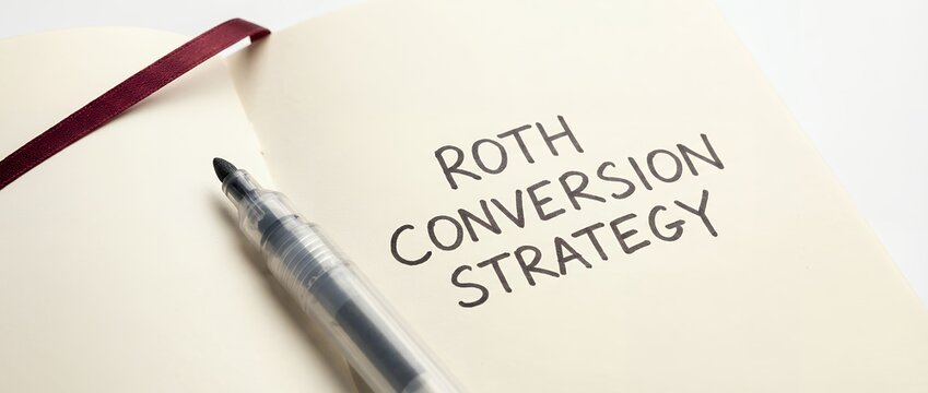 Open notebook page with handwritten text ROTH CONVERSION STRATEGY and a marker pen beside a burgundy ribbon finance investment retirement savings planning money taxes accounting
