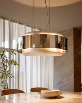 Round chrome pendant lamp above a dining table with marble accents