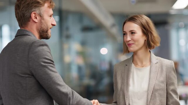 Business meeting between smiling businessman and businesswoman shaking hands in modern office environment