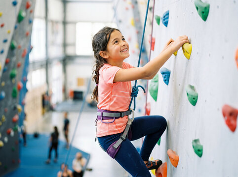 Happy young girl climbing indoor rock wall with safety rope