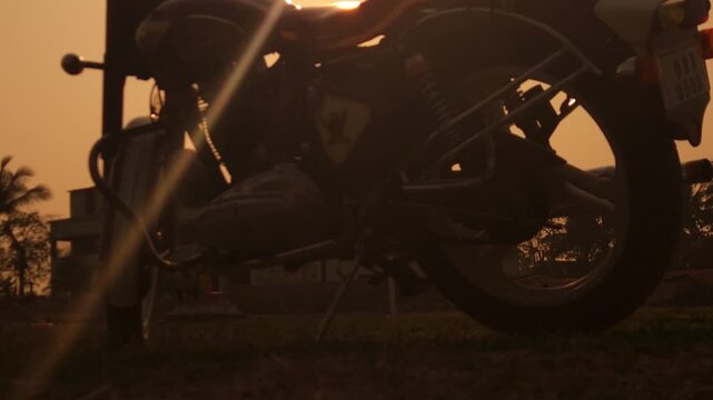 Motorcycle silhouette at sunset with golden hour light, bike parked against orange sky with sun rays and palm trees, scenic travel landscape representing freedom, adventure, road trip lifestyle and ou