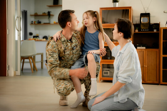 Happy military father in uniform returning home hugging his young daughter while smiling mother watches, emotional family reunion, love, support, homecoming moment, lifestyle outdoor scene