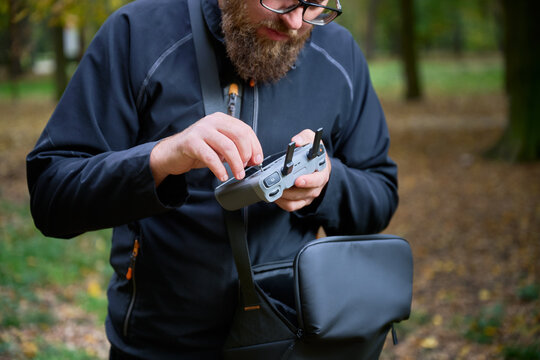 Man adjusts drone controller and checks settings before flight. Bearded man preparing remote control in a park, setting up equipment for aerial photography and filming