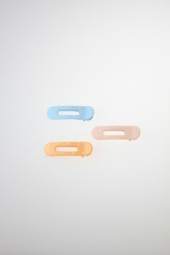 Three pastel hair clips rest against a clean white background. Soft hues include blue, peach, orange. Minimalist design suits modern fashion trends. Ideal for beauty, lifestyle, minimalist composition