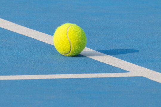 Tennis ball sits on bright blue court, framed by white lines