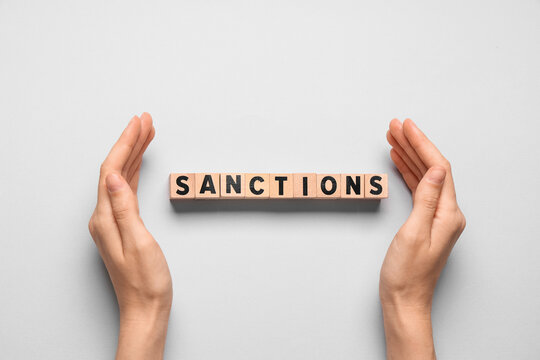 Female hands and word SANCTIONS on white background