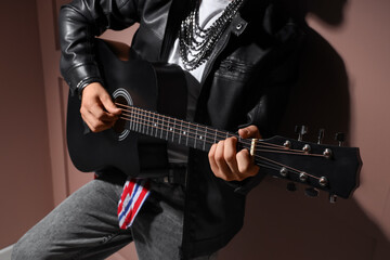 Obraz premium Young man in leather jacket playing guitar on brown background