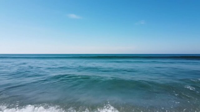 Clear blue ocean waves gently rolling onto the shore under a bright, cloudless sky on a sunny day, creating a serene and tranquil seascape