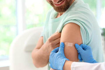 Obraz premium Young man receiving medical patch from doctor after vaccination in clinic, closeup