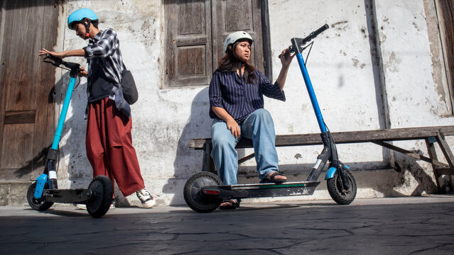 Brother and sister using  electric scooter and safety helmet with old house in the city when travelling 