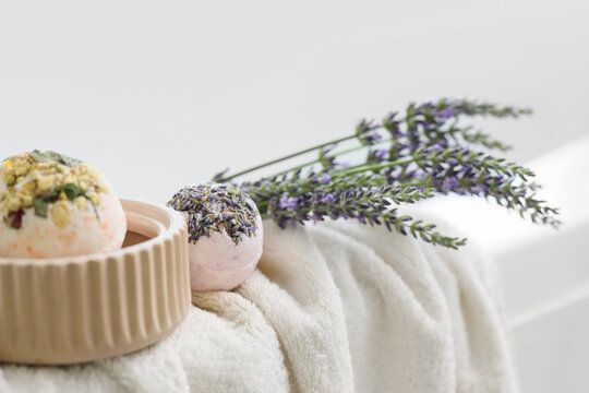 Floral bath bombs with lavender flowers and towel on bathtub in bathroom