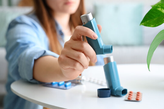 Woman taking modern inhaler from table with pills in living room