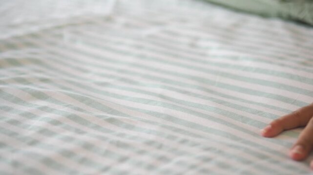 Hand touches soft bed sheet in quiet bedroom