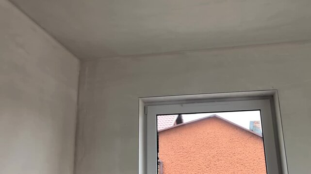 White plastered walls in empty room. Close up of renovation site with metal profiles and window. Panning right on unfinished interior ceiling and walls. Candid construction background.
