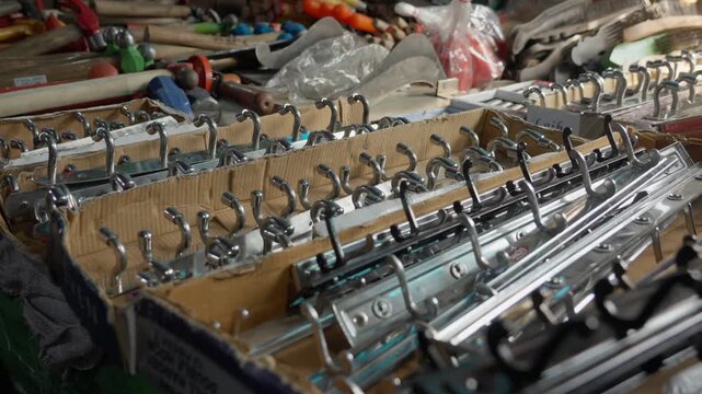 A closeup shot of various chrome and metal wall hooks displayed in cardboard boxes at a local hardware stall in Indian street market.