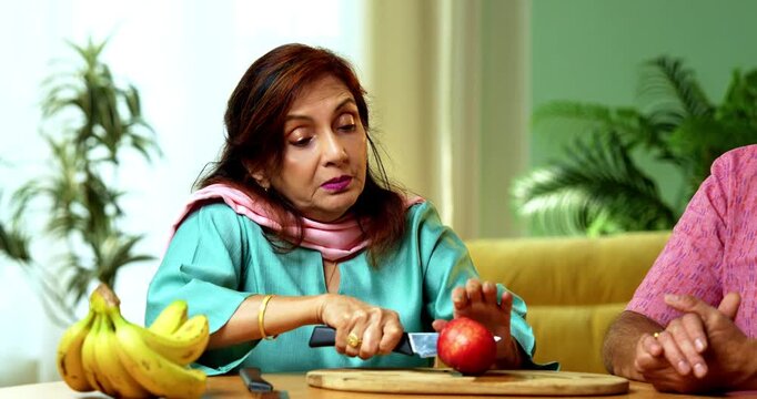 Senior Indian woman cuts a fresh apple and gives a slice to her husband as they both enjoy the healthy fruit and smile together in their modern kitchen