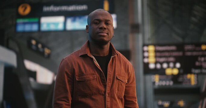 Male African American Stands With Confidence and Subtle Smile in Departure Area of International Airport. Bustling Environment Terminal, With People Walking, Highlights Man Focused Demeanor. Portrait.