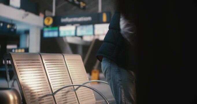 Man Carrying Backpack and Pulling Suitcase, Approaches Seating Area in Airport Terminal. Sits Down on Metal Bench, Leans Back, and Immediately Takes Smartphone Out of Pocket to Check Notifications.