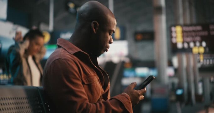 Sitting in Departure Lounge, Man Verifies Flight Details. Male Scans Ticket on Smartphone and Repeatedly Looks Up at Large Terminal Display Board FIDS to Cross Reference Gate Number and Boarding Time.