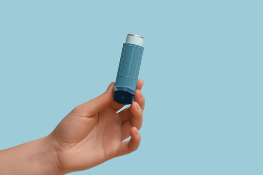 Female hand with modern asthma inhaler on blue background