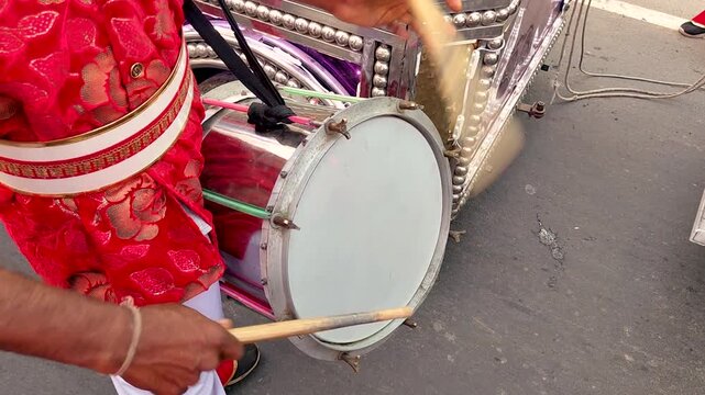 Hands playing drum on street during festival or parade, rhythmic motion, cultural percussion, natural sunlight highlights, energetic outdoor performance