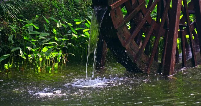 Close-up of a traditional wooden waterwheel operating in a garden pond.
