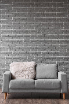 Sofa with fur mat near grey brick wall in room