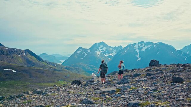 Middagsfjellet, Sandland, Nordkapp, Finnmark, Norway - Two Hikers and Their Dogs Pause to Admire the Snow-capped Mountain Landscape - Static Shot