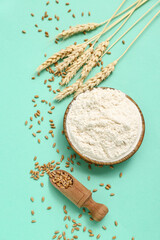 Naklejka premium Bowl with wheat flour, scoop and spikelets on turquoise background