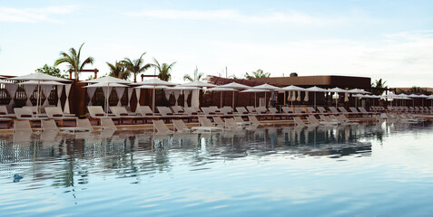 Fototapeta premium A comprehensive view of an elegant pool area lined with sun loungers and umbrellas against a clear blue sky, inviting guests for leisure and relaxation in a serene environment.