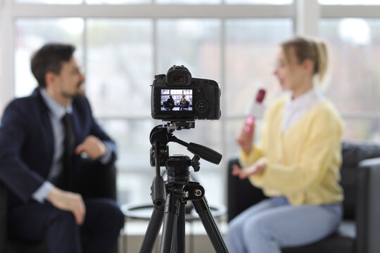 Female journalist with microphone having an interview with man on camera screen in office, closeup