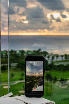 A smartphone captures a stunning coastal sunset over waves, showcasing the beauty of nature, reflections, and vibrant colors against a serene landscape in the background.