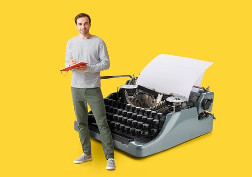Young man with notebook and big typewriter on yellow background