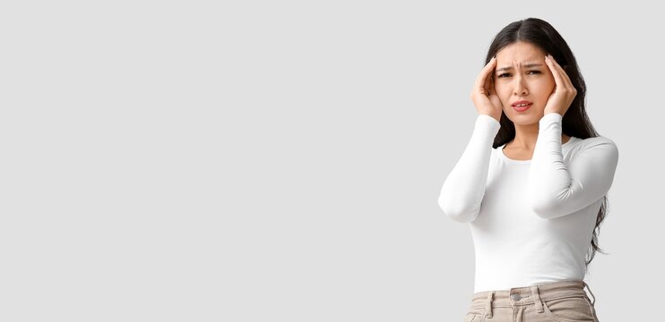 Young Asian woman suffering from headache on light background with space for text