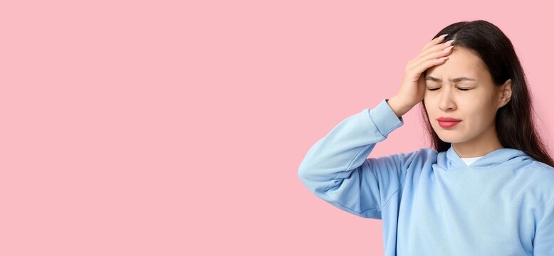 Young Asian woman suffering from headache on pink background with space for text
