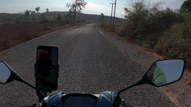 POV riding a scooter or motorbike in Laos on a bitumen road through the summer period with a blue bag strung over the front of the bike and a phone mount.