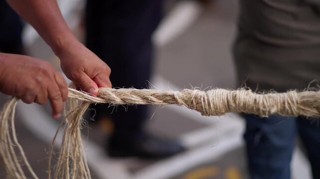 Closeup of hands twisting natural fiber rope by hand traditional rope making craft, braiding in slow motion