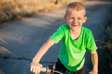 Obraz premium Happy young boy with blond hair riding a bicycle on a sunny day. Summer walk. Childhood. Holidays