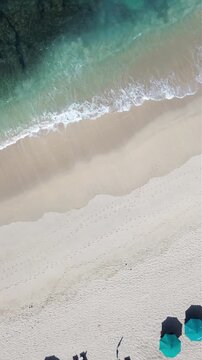 Aerial view of the pristine Mawun Beach in Lombok, Indonesia, featuring turquoise crystal clear waters, white sandy coastline, and lush tropical hills under a bright sunny sky.